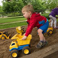 A child pushes a toy dump truck through a sandbox.